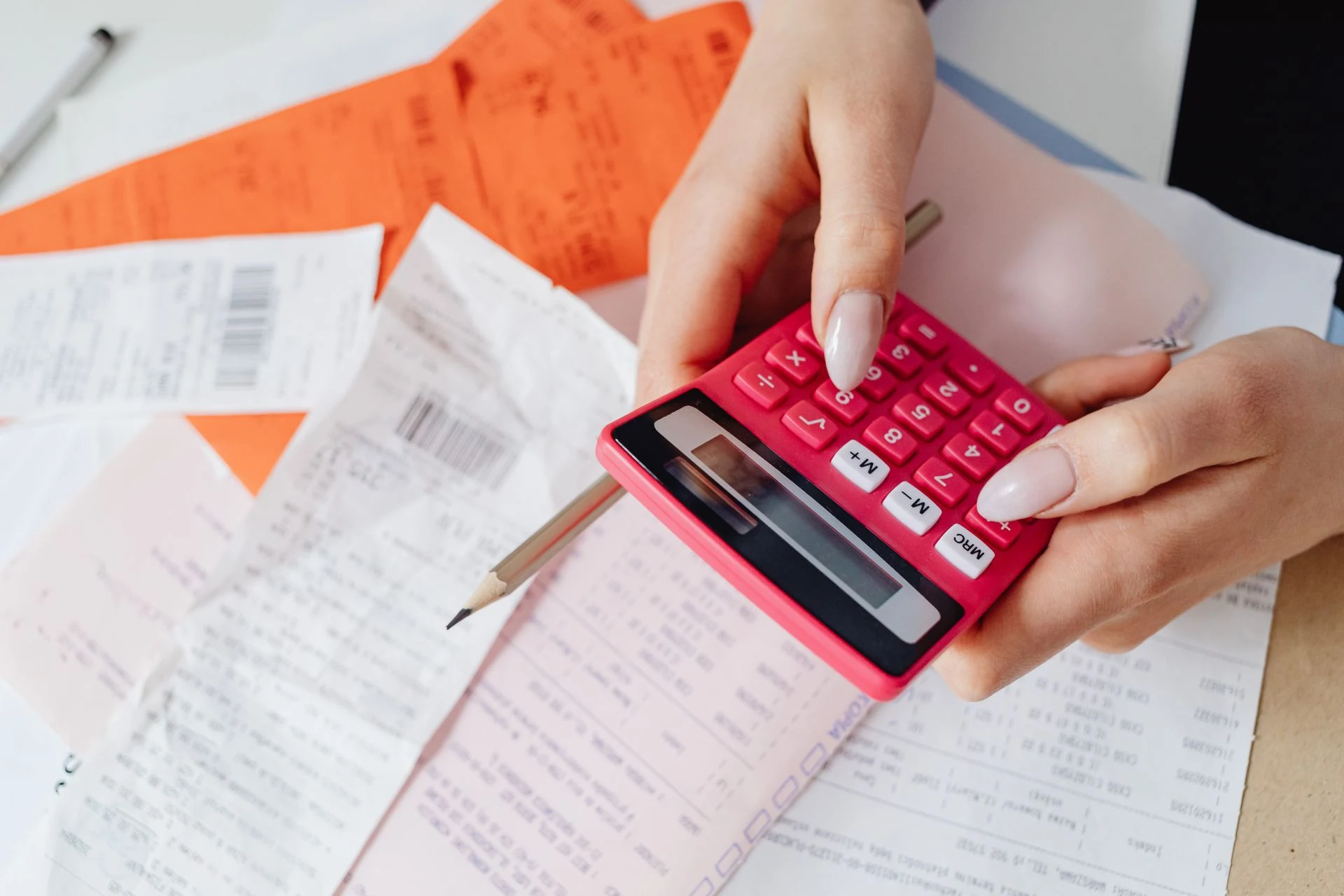 Hand using a red calculator on top of printed bills and receipts