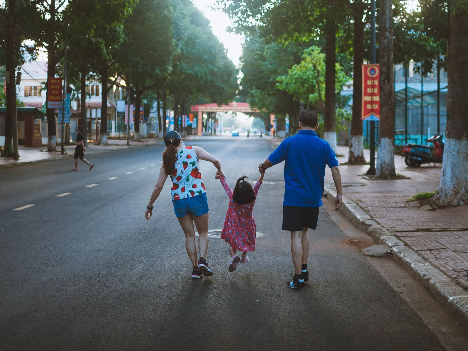 Parents walking down a street holding a young child's hands