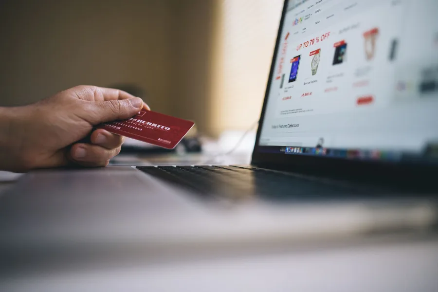Hand holding a bank card in front of a laptop