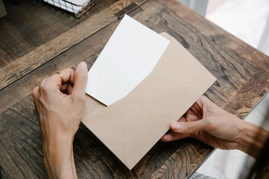 Hands opening a brown envelope on a wooden table