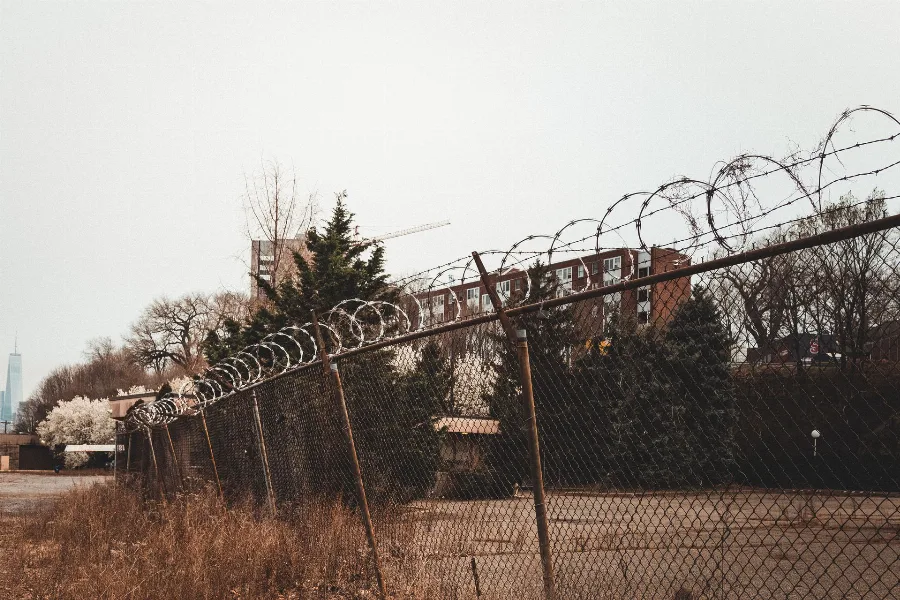 Razor wire on top of a perimeter fence with buildings behind it