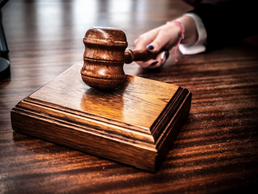 Judge's hand resting beside a wooden gavel on a desk