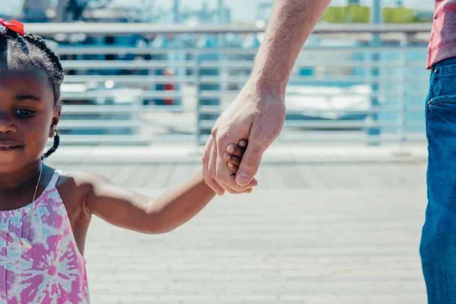 Adult holding a young child's hand outdoors