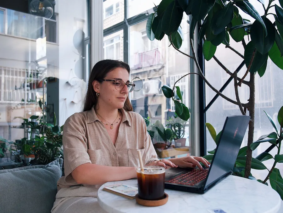 Woman working on a laptop at a cafe table by a window