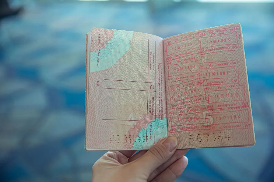 Hand holding an open passport with entry and exit stamps inside an airport terminal