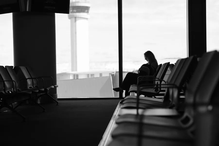 Silhouette of a passenger sitting alone in an airport terminal waiting area