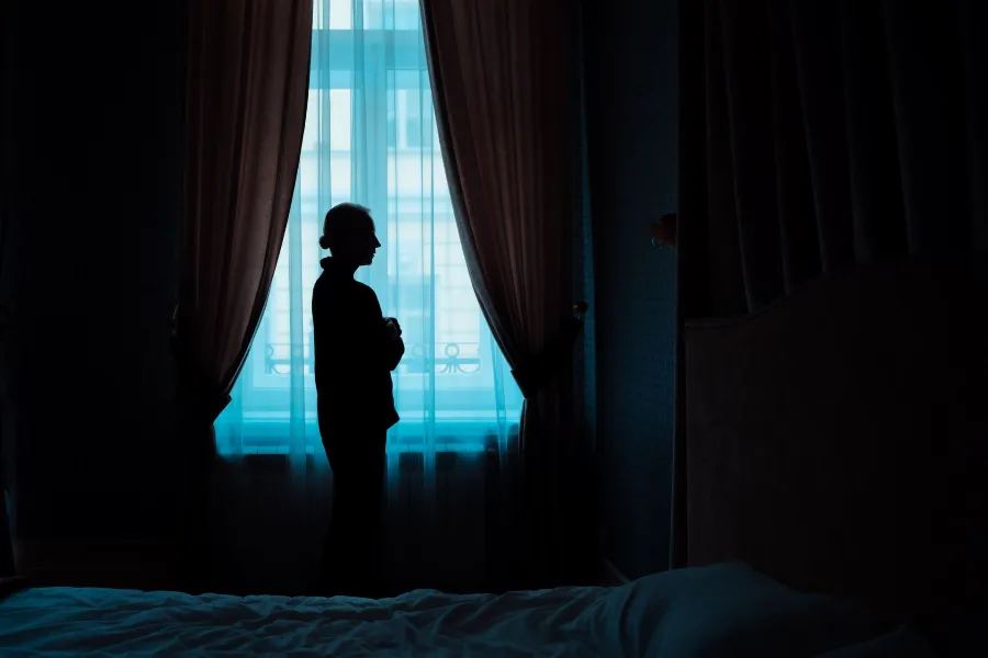 Silhouette of a woman standing at a curtained window