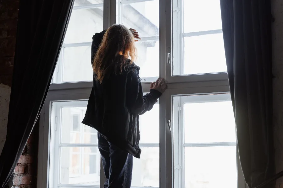 Woman standing at a tall window looking outside
