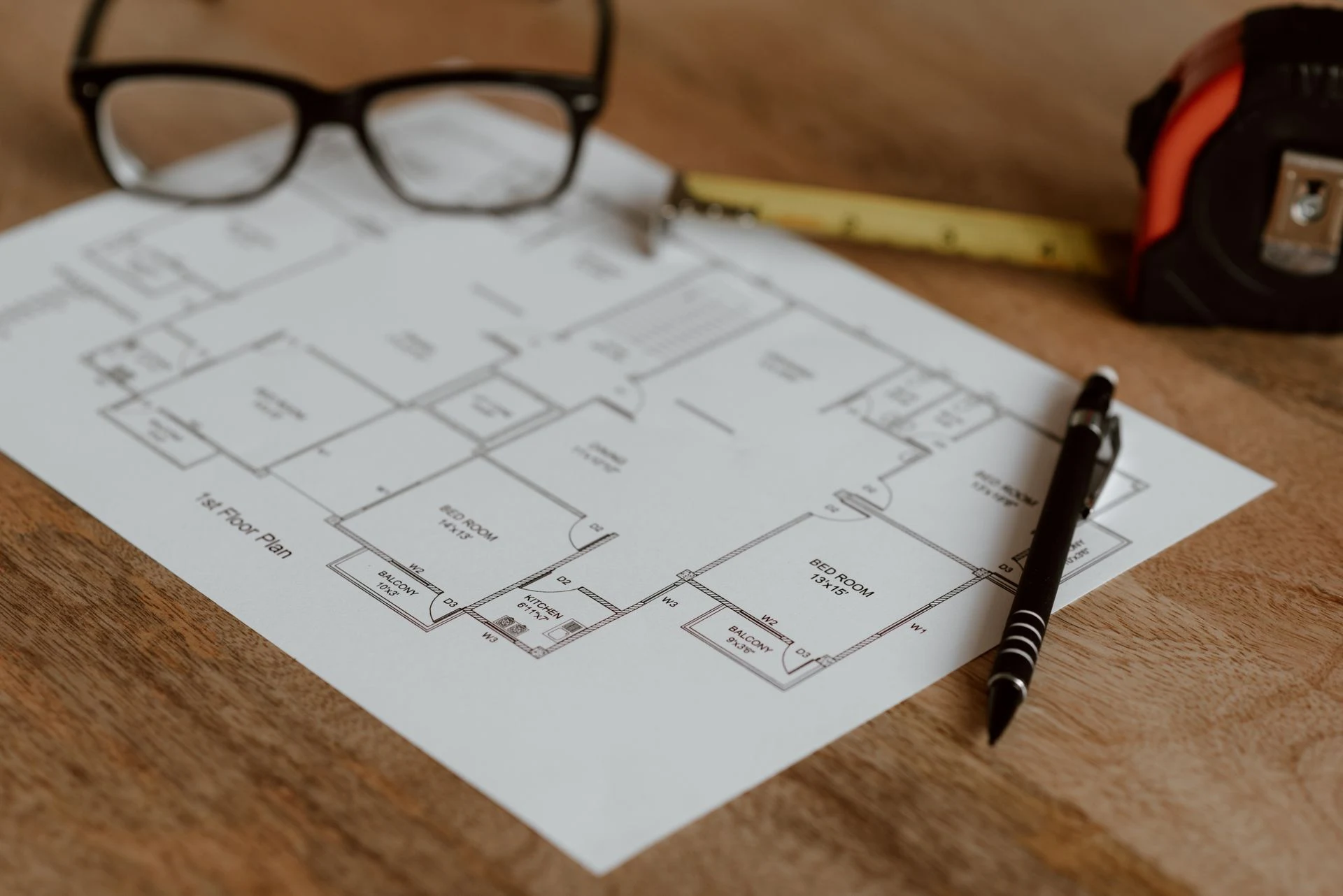 Architectural floor plans, glasses and a pen on a wooden desk