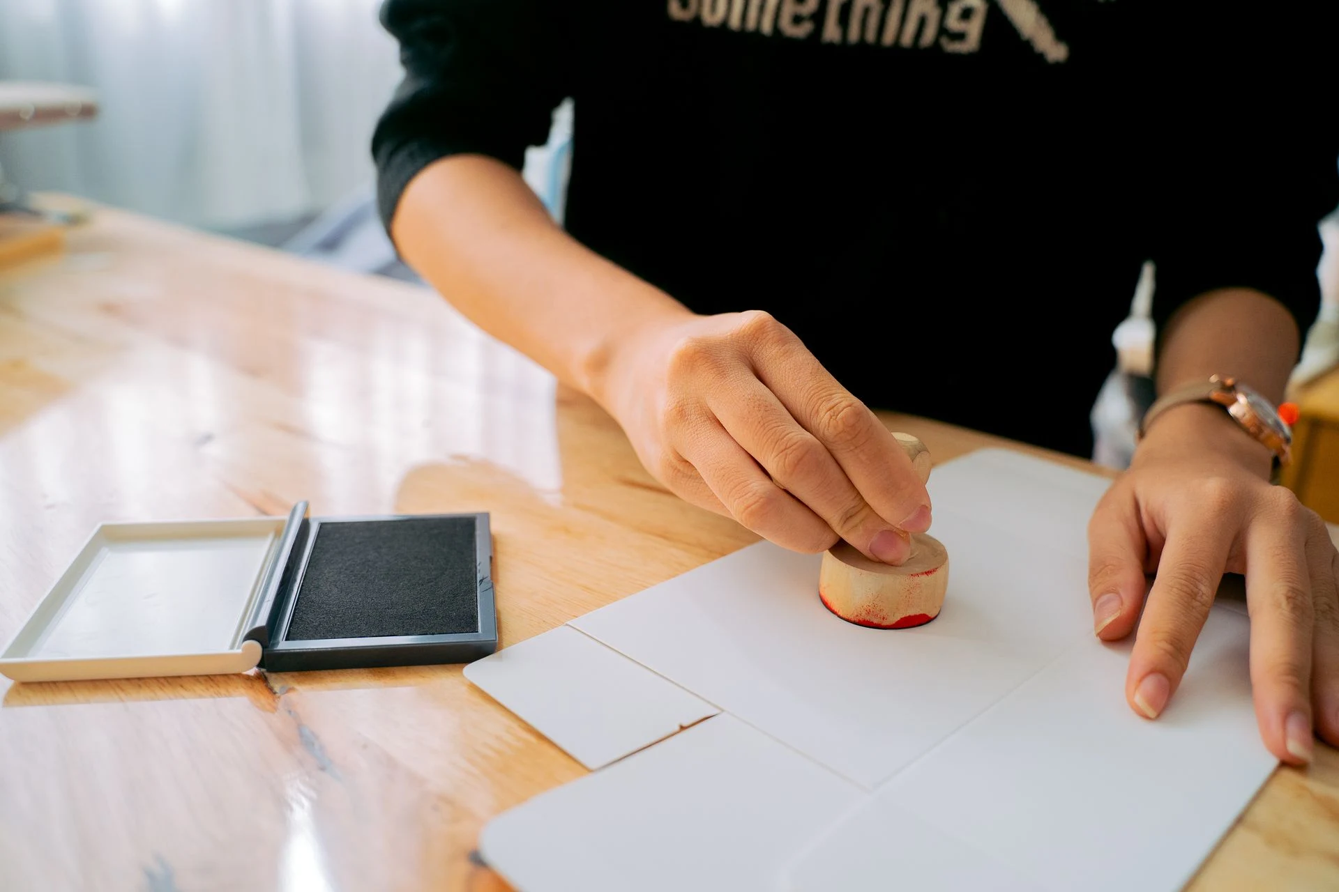 Hand pressing a rubber stamp onto a sheet of paper at a desk