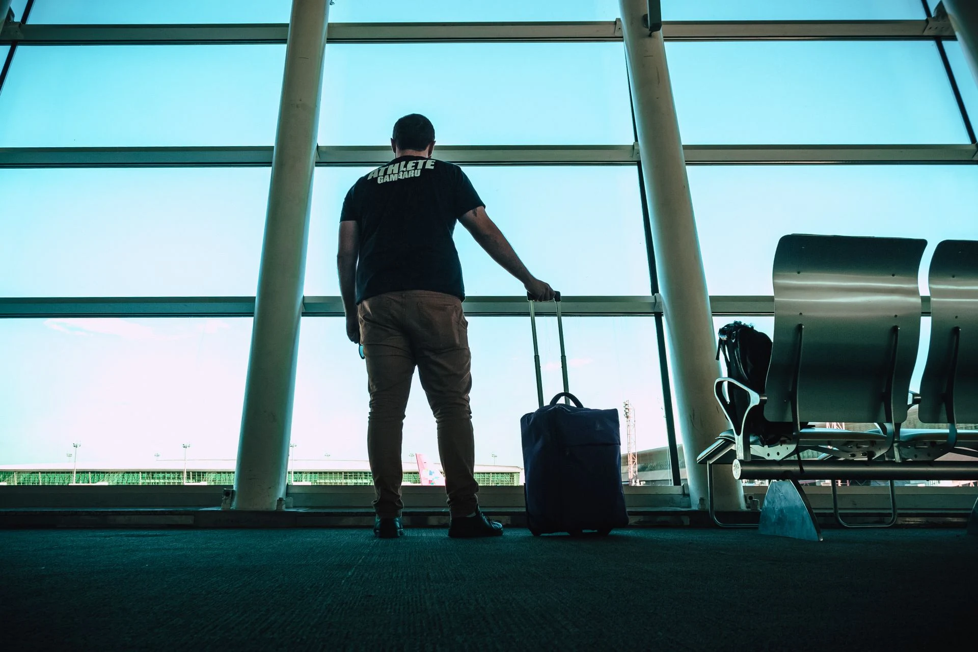 Traveller with a suitcase standing at an airport window looking out